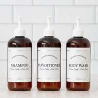 Amber PET set of refillable bottles with white pumps and coordinated labels for the shower.