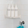 Tall white plastic set of shower bottles with white pumps and silkscreen print for shampoo, conditioner, and body wash, on shower shelf.