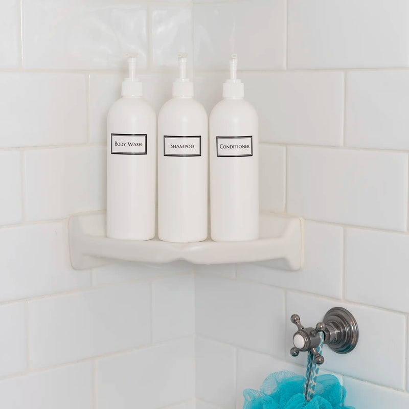 Tall white plastic set of shower bottles with white pumps and silkscreen print for shampoo, conditioner, and body wash, on shower shelf.
