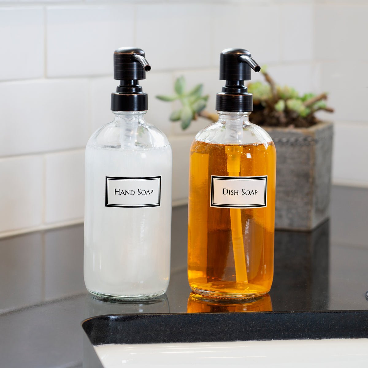 Set of two clear glass Boston round bottles with permanent ceramic printed text for "Hand Soap" and "Dish Soap". With oil rubbed bronze pumps.
